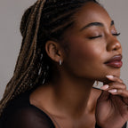 Woman with braided hair and opal hoop earrings resting her head on a hand against a neutral background