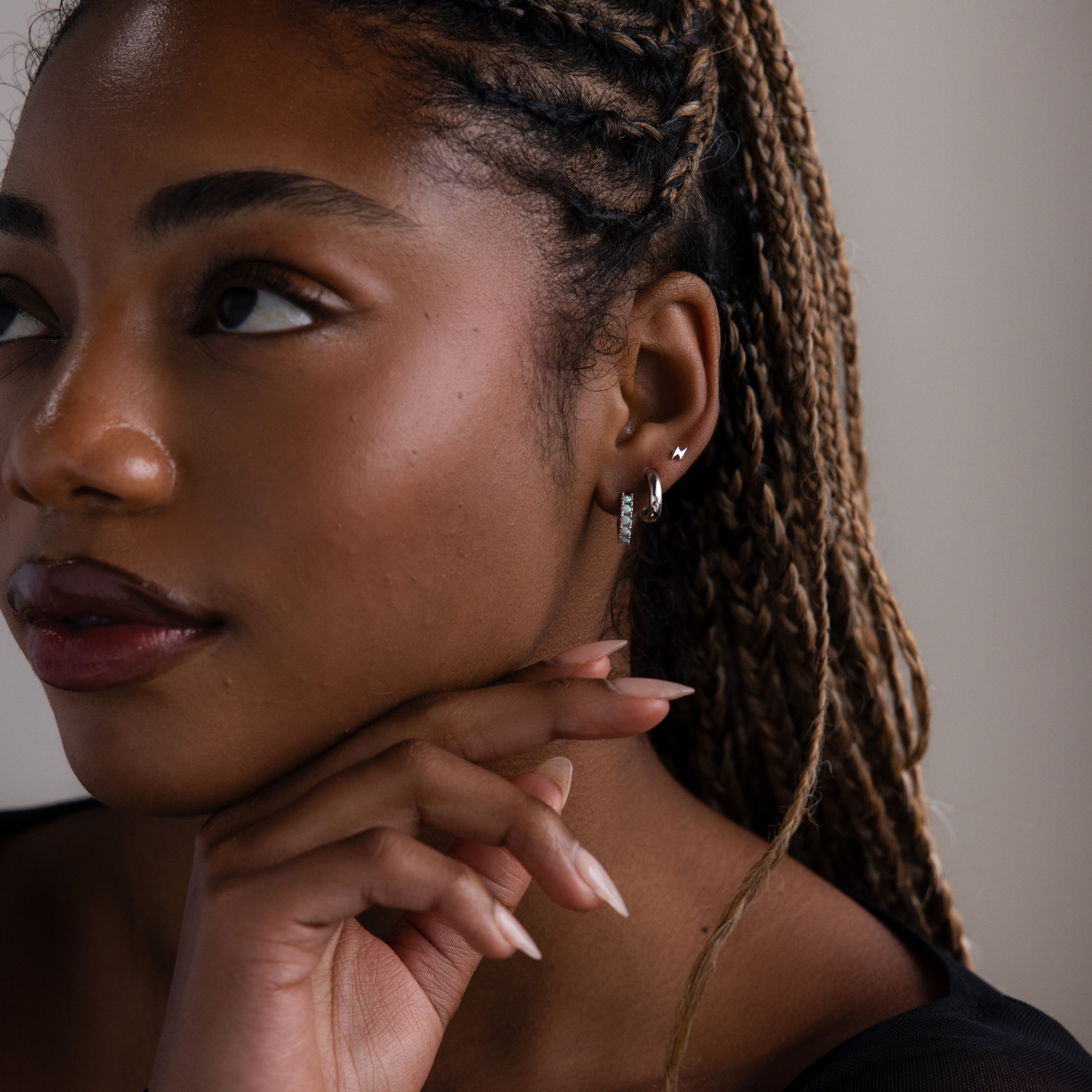 Close-up of a woman with braided hair, multiple silver earrings, and a neutral background