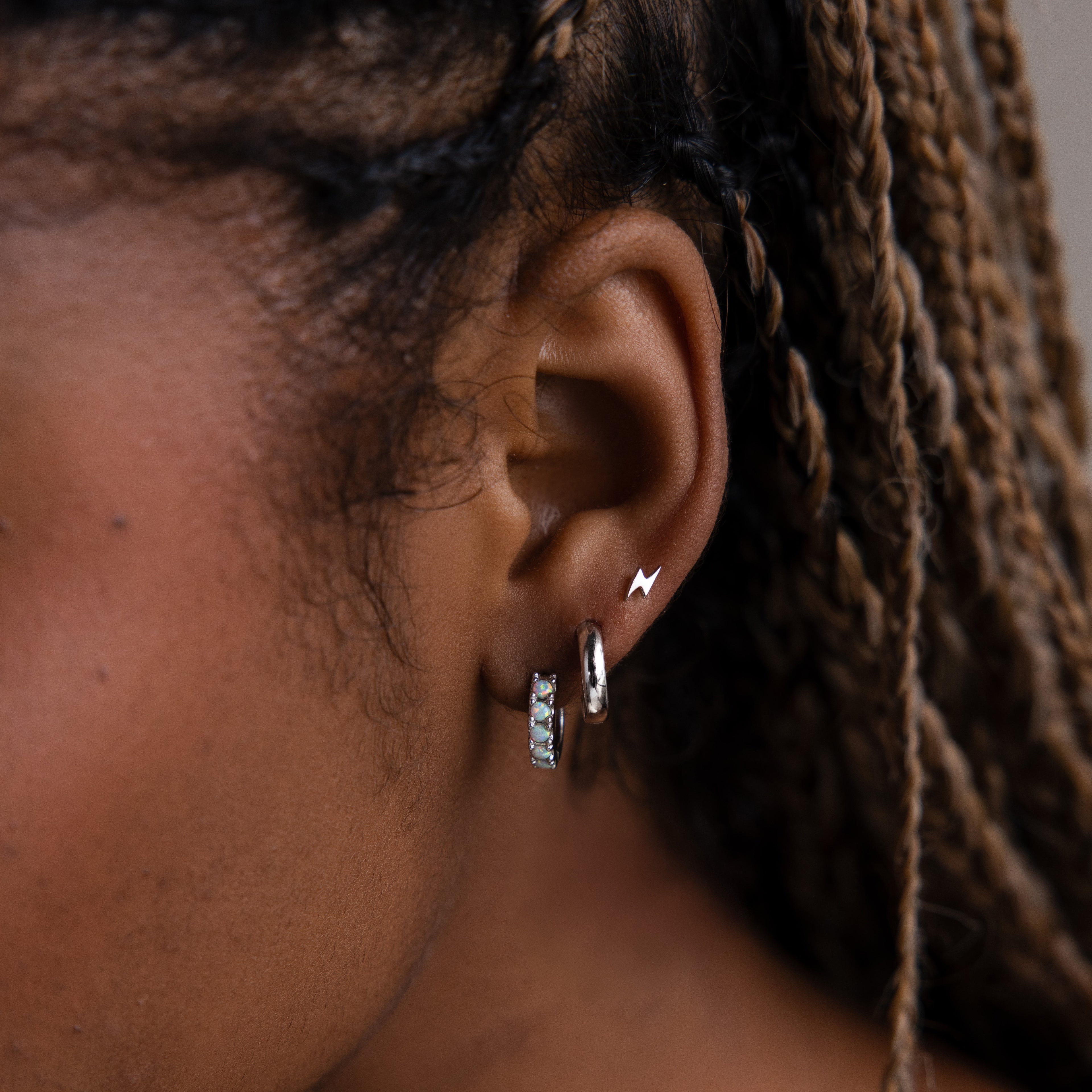 Close-up of a model with various silver earrings against a blurred background