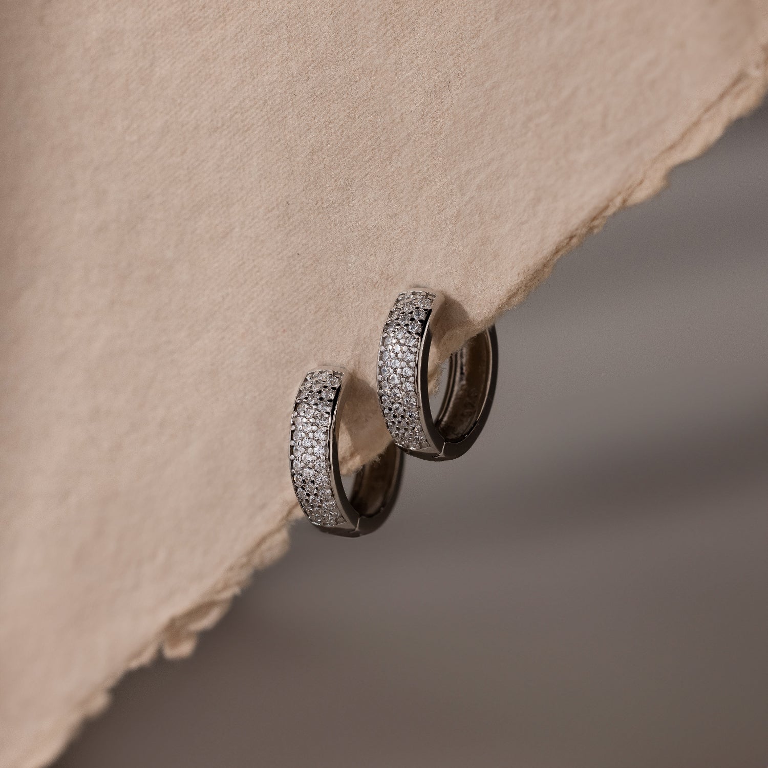 Pair of silver hoop earrings on a textured beige surface
