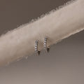 Pair of silver diamond hoop earrings on a beige fabric background