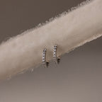 Pair of silver diamond hoop earrings on a beige fabric background