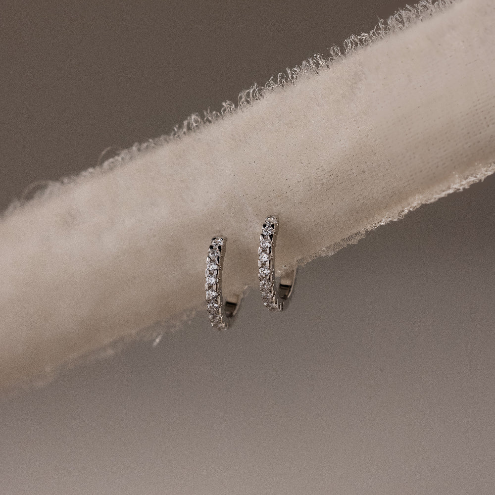 Pair of silver diamond hoop earrings on a beige fabric background