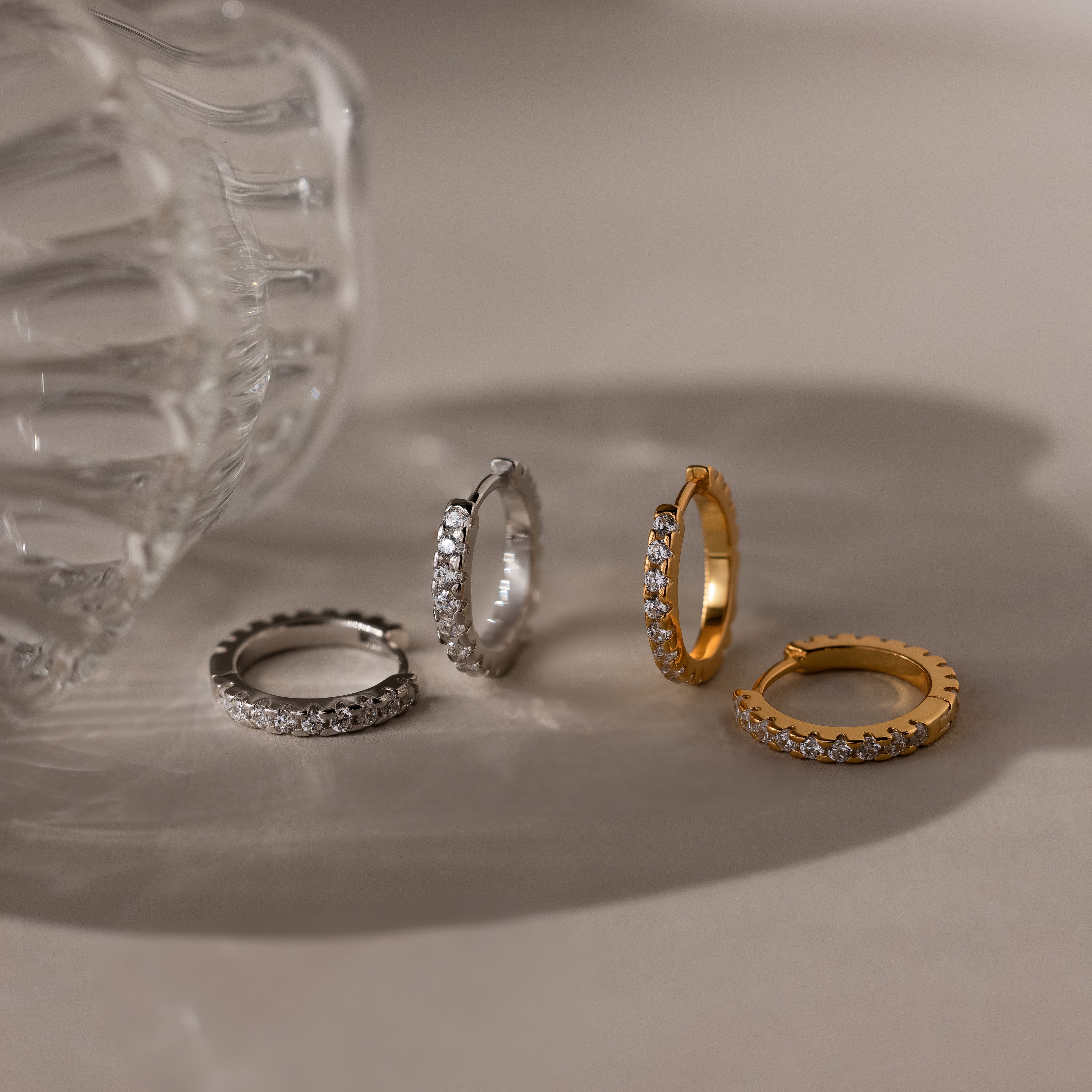 Two pairs of gold and silver diamond hoop earrings on a neutral background
