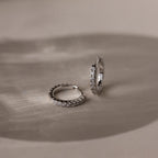 Pair of silver diamond hoop earrings on a textured beige surface