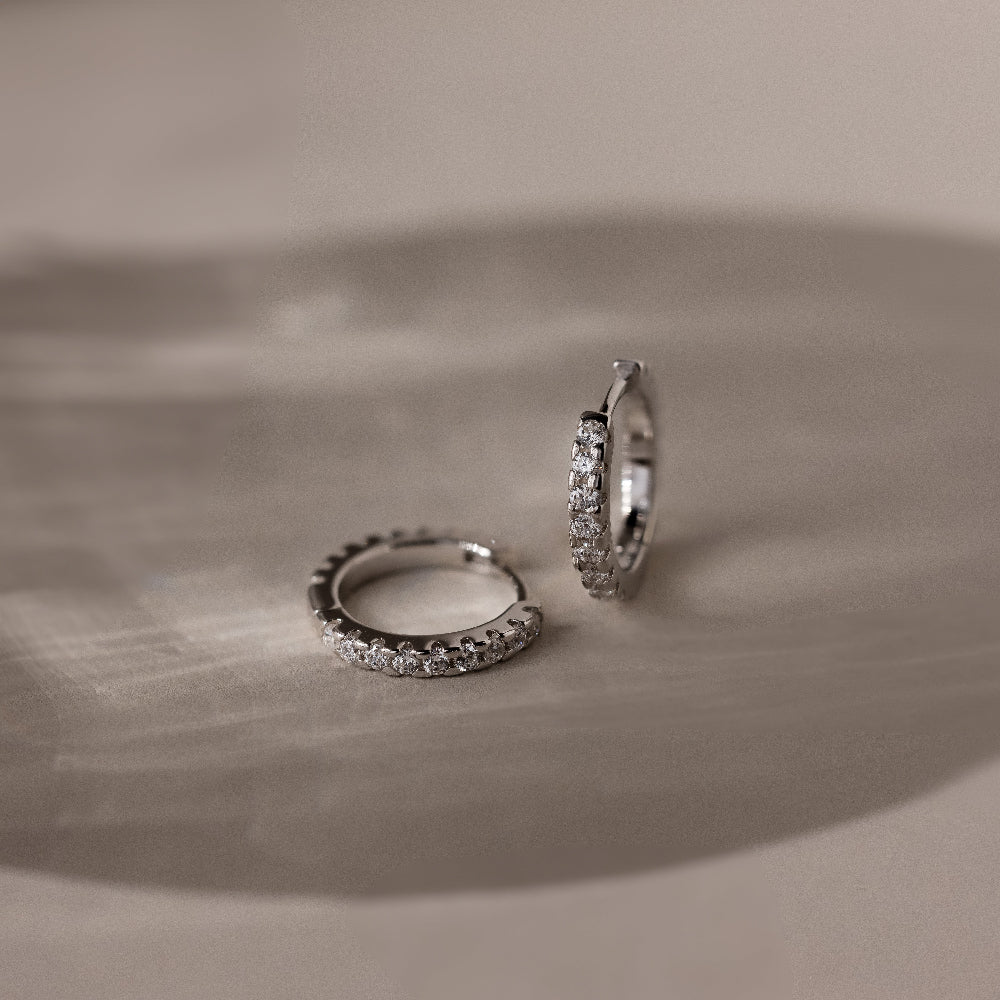 Pair of silver diamond hoop earrings on a textured beige surface