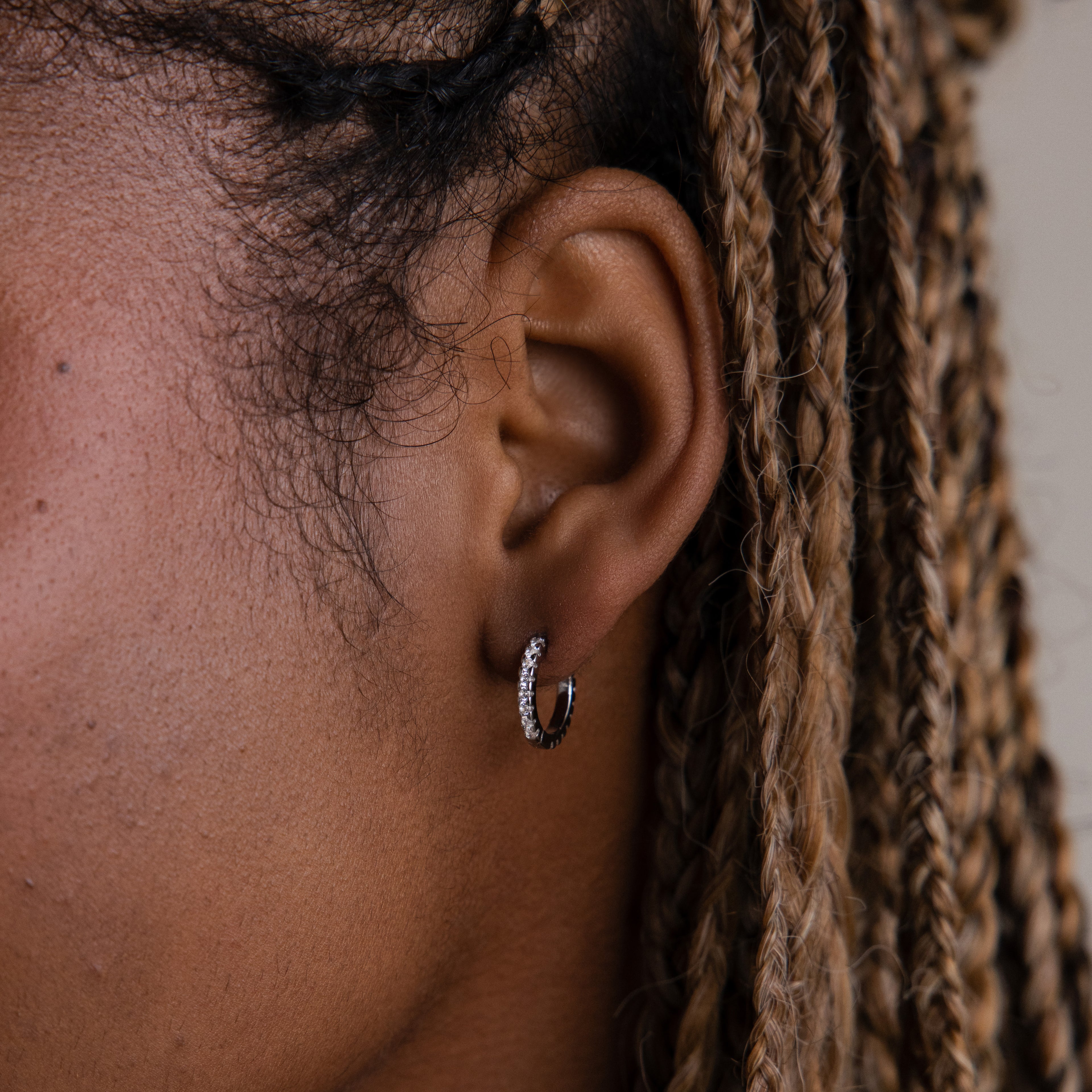Close-up of an ear with braided hair wearing a silver diamond hoop earring.
