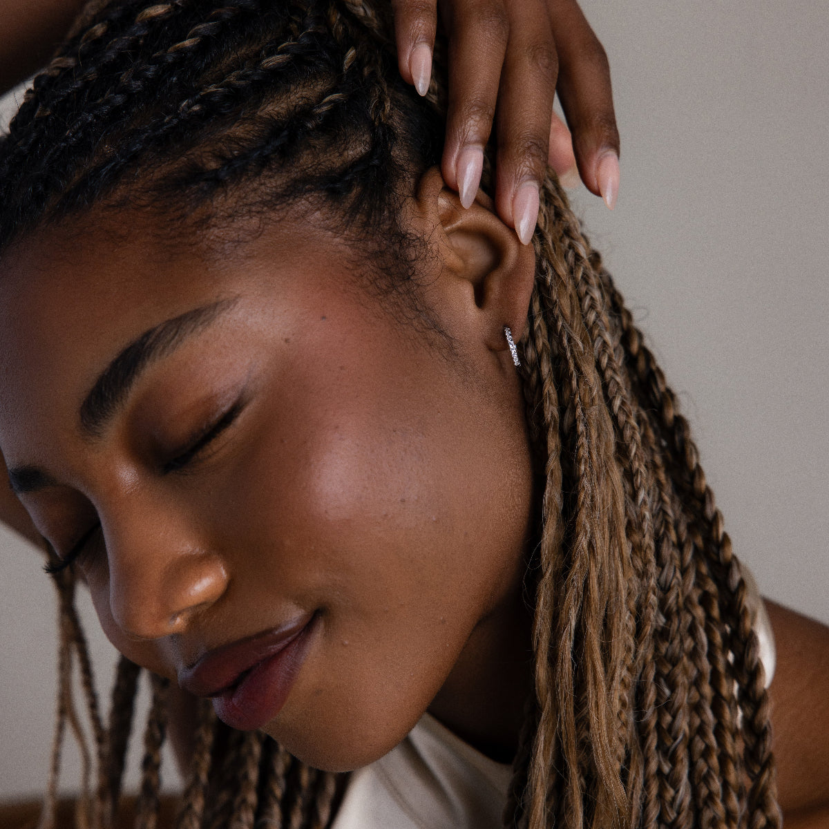 Woman with braided hair and a silver hoop earring touching her head, wearing a white top.