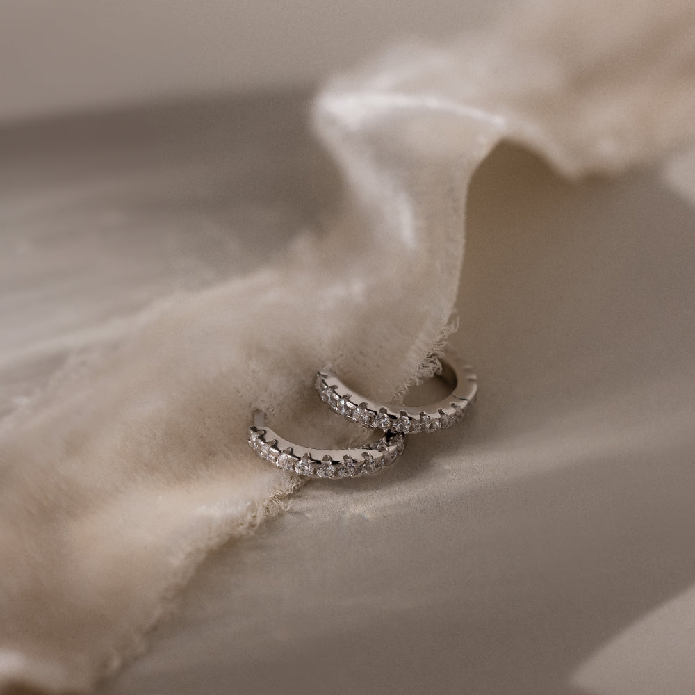 Pair of silver pave hoop earrings on beige fabric