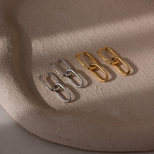 Four gold and silver chain-style hoop earrings on a textured beige surface.