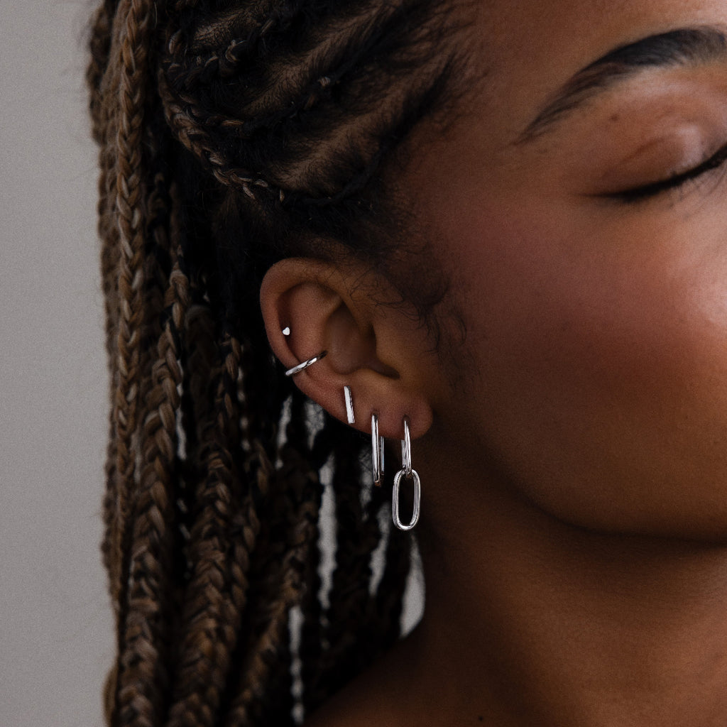 Close-up of a person's ear with multiple silver earrings against a neutral background