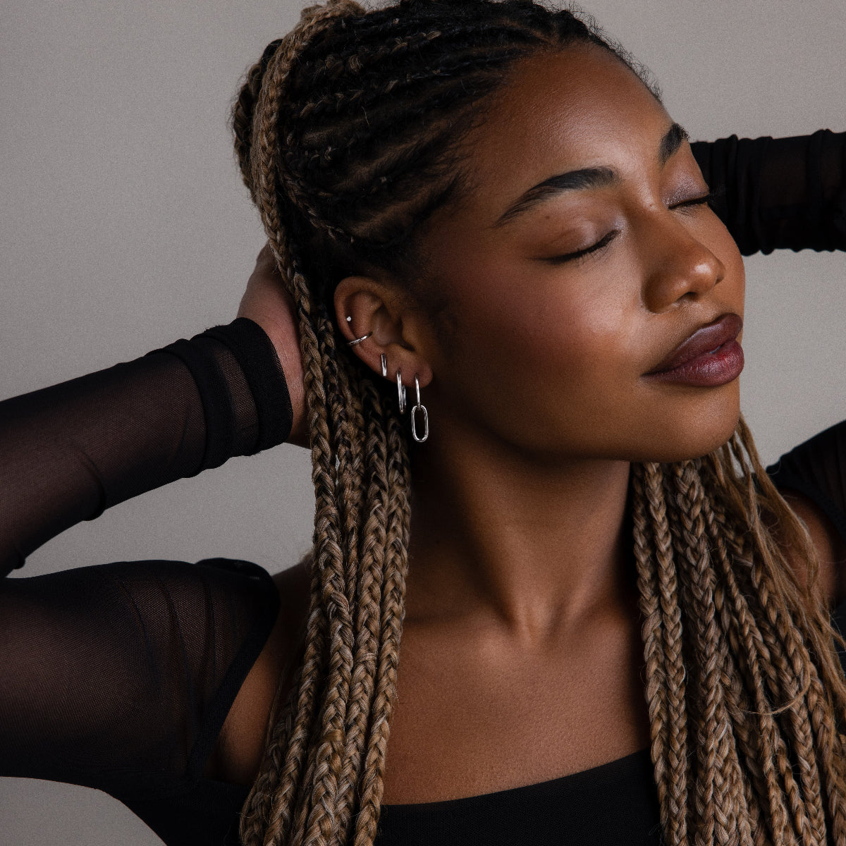 Woman with braided hair wearing various silver earrings against a neutral background