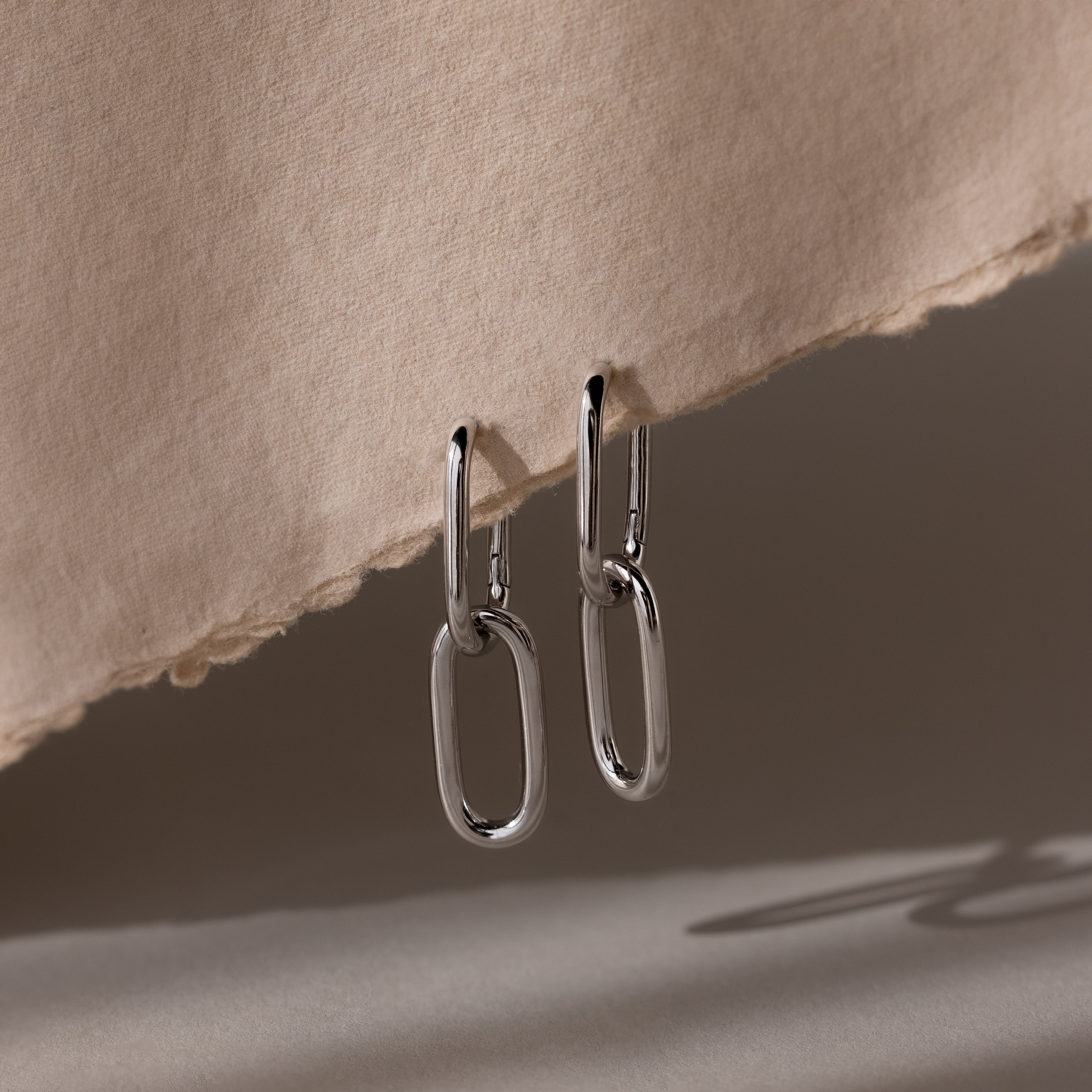 Silver linked hoop earrings on a textured beige surface
