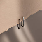 Metallic silver rectangular hoop earrings attached to a piece of beige paper against a gradient background