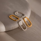 Four metallic silver and gold rectangular hoop earrings on a textured surface