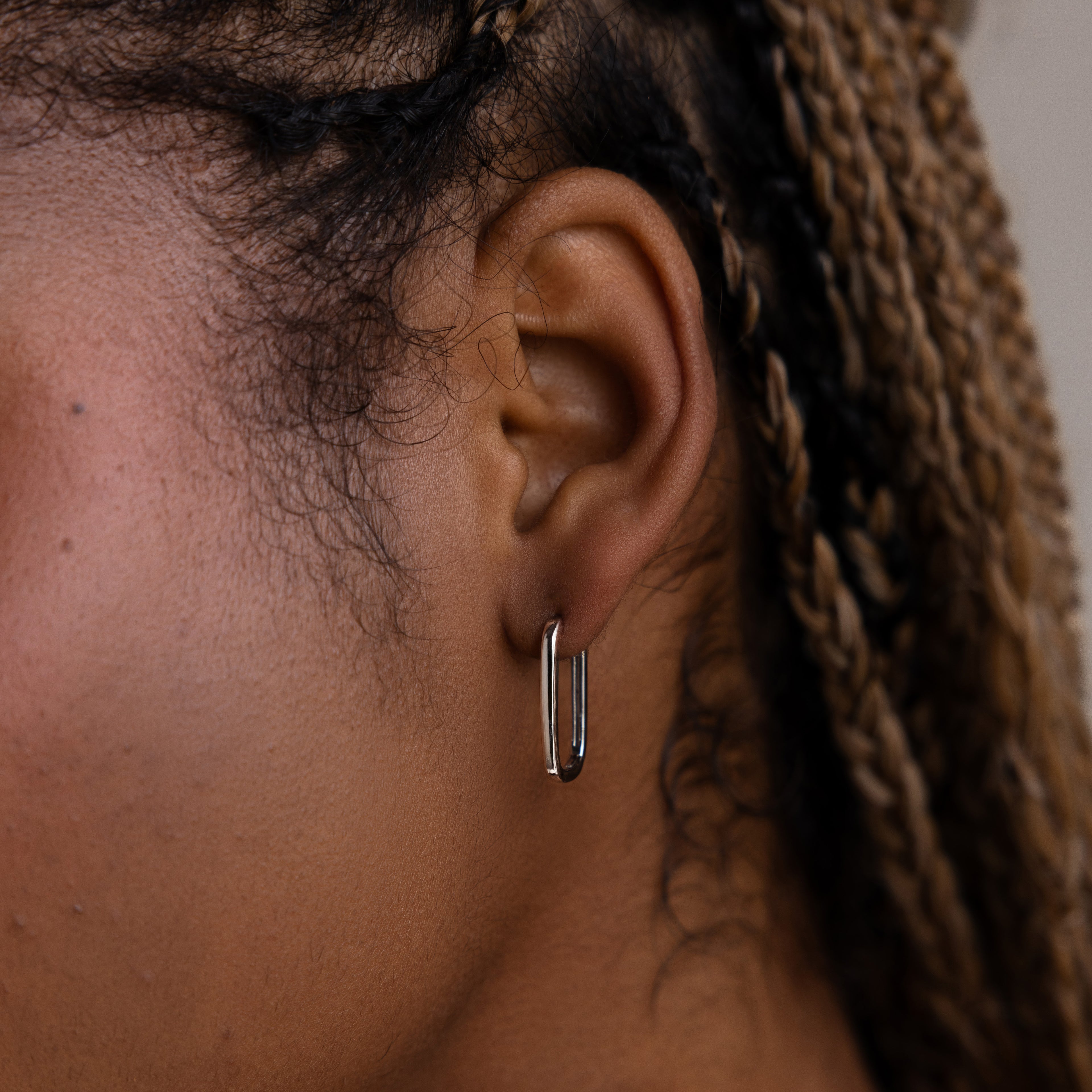 Close-up of an ear wearing a silver rectangular hoop earring with braided hair.