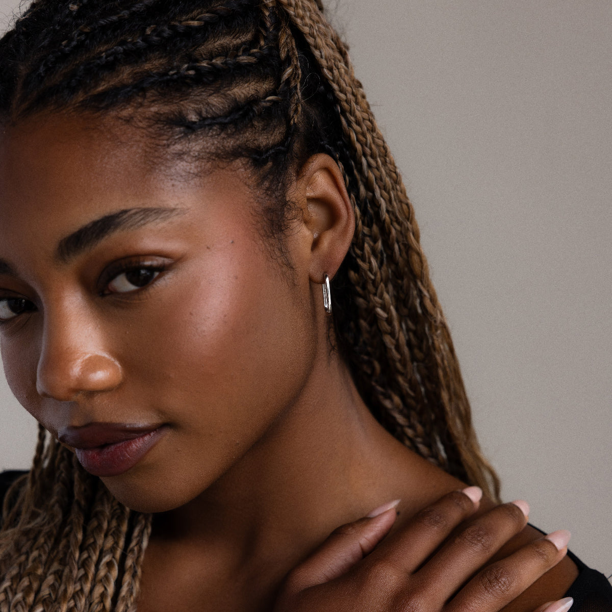 Close-up of a woman with a silver hoop earring and braided hair against a neutral background
