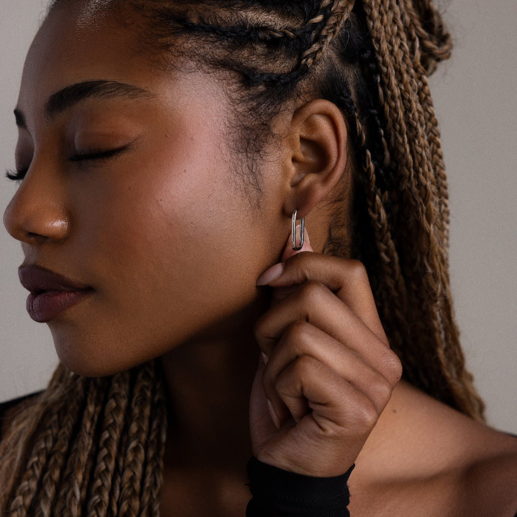 Close-up of a woman adjusting a silver rectangular hoop earring with braided hair.