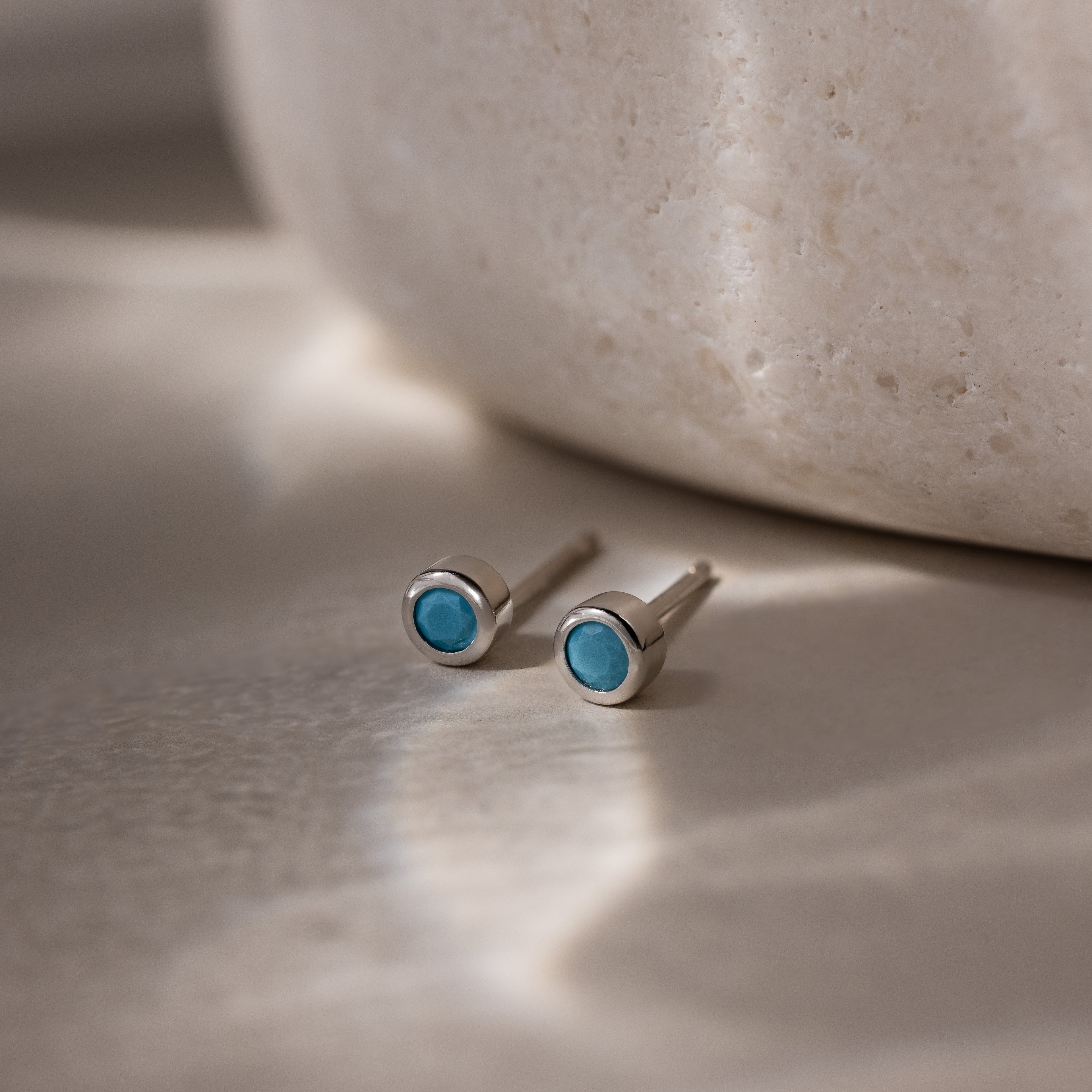 Pair of silver earrings with turquoise stones on a neutral background