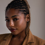 Woman with braided hair wearing a brown jacket and silver turquoise stud earrings against a neutral background