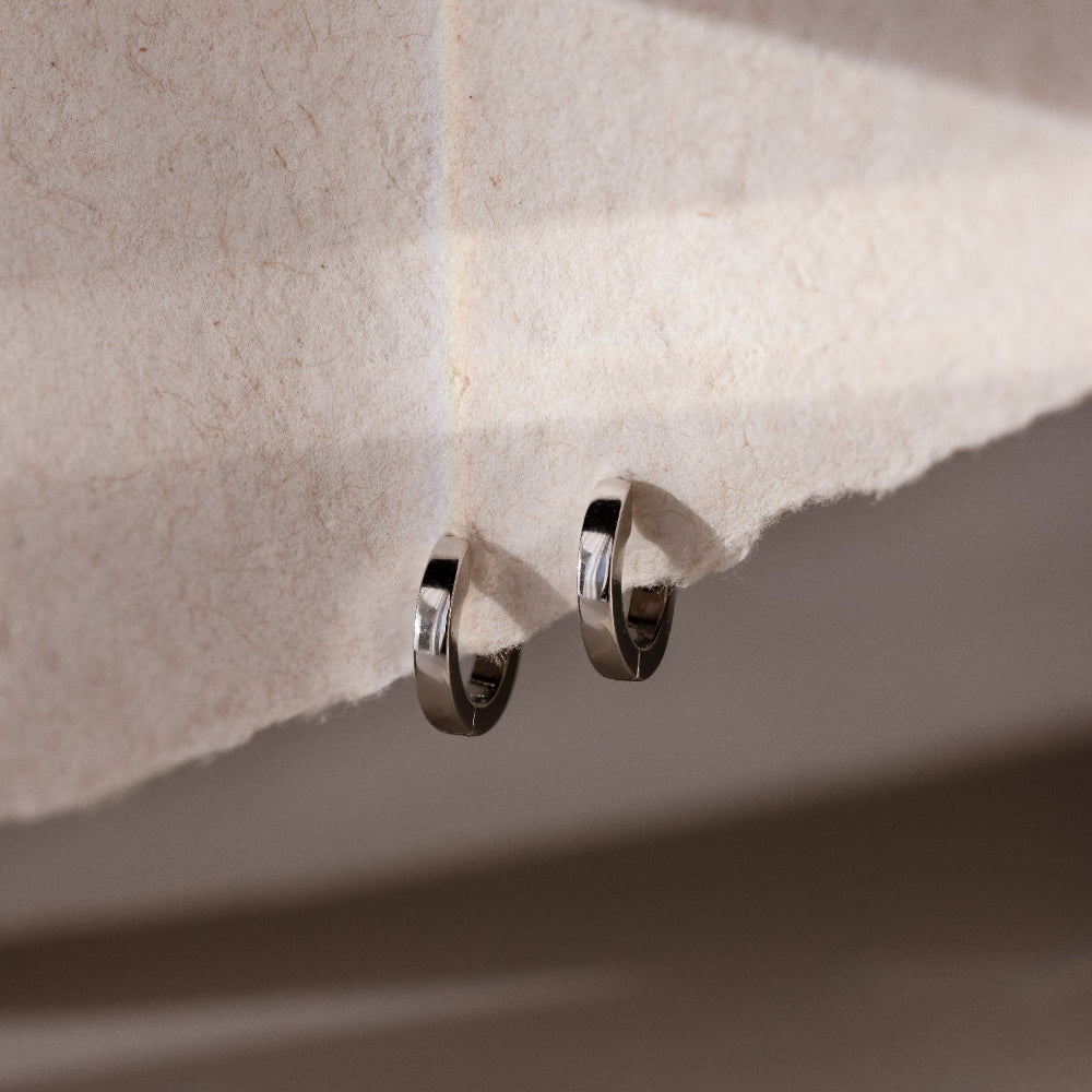 Silver hoop earrings on a textured beige surface