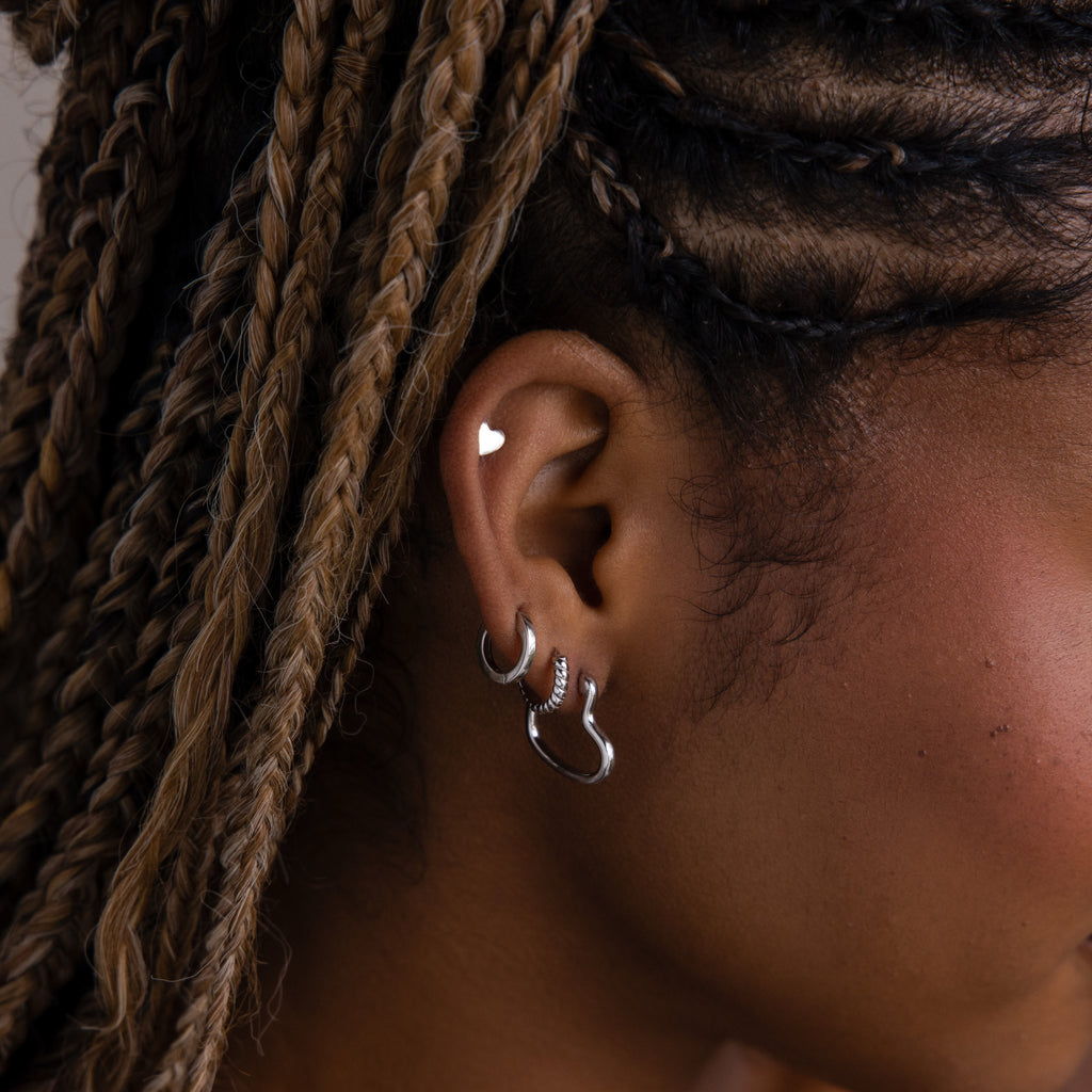 Close-up of an model with silver hoop earrings, a silver heart shaped stud earring, and braided hair.