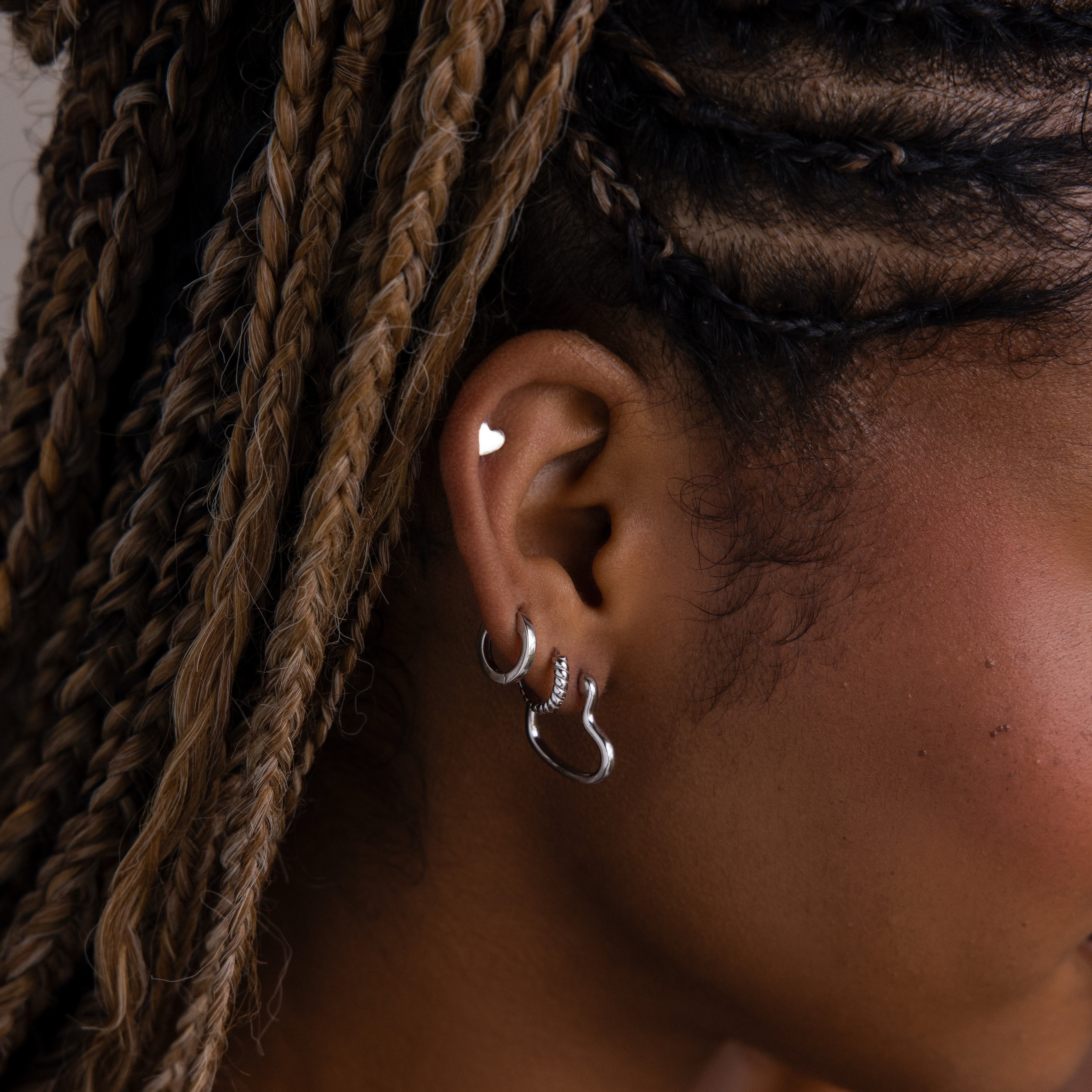 Close-up of an model with silver hoop earrings, a silver heart shaped stud earring, and braided hair.