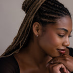 Woman with braided hair and a silver hoop earring resting her head on her hand against a neutral background