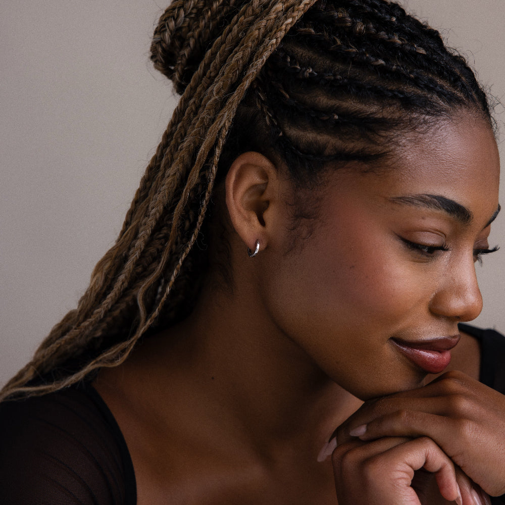 Woman with braided hair and a silver hoop earring resting her head on her hand against a neutral background