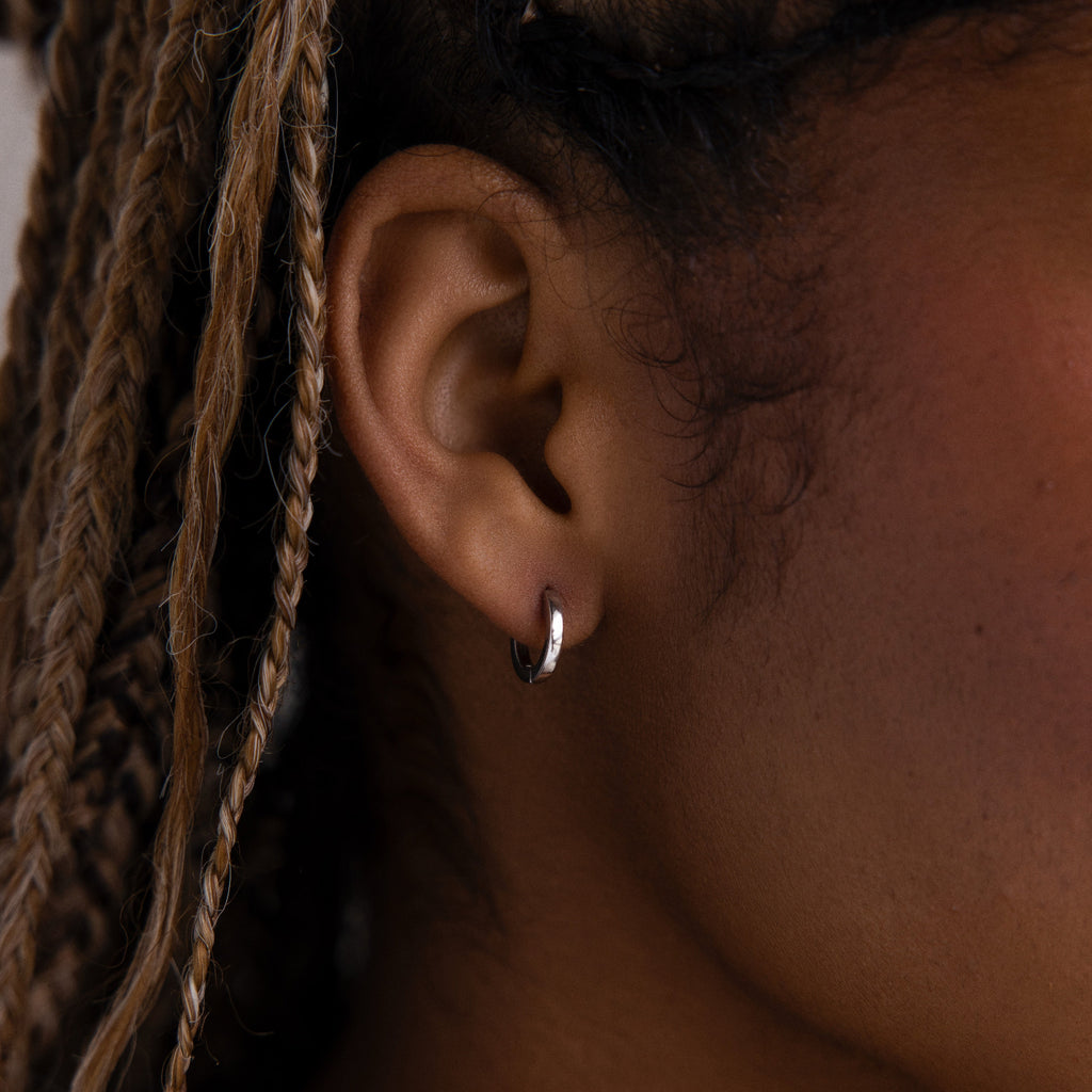 Close-up of an ear with a silver hoop earring and braided hair.