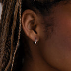 Close-up of an ear with a silver hoop earring and braided hair.