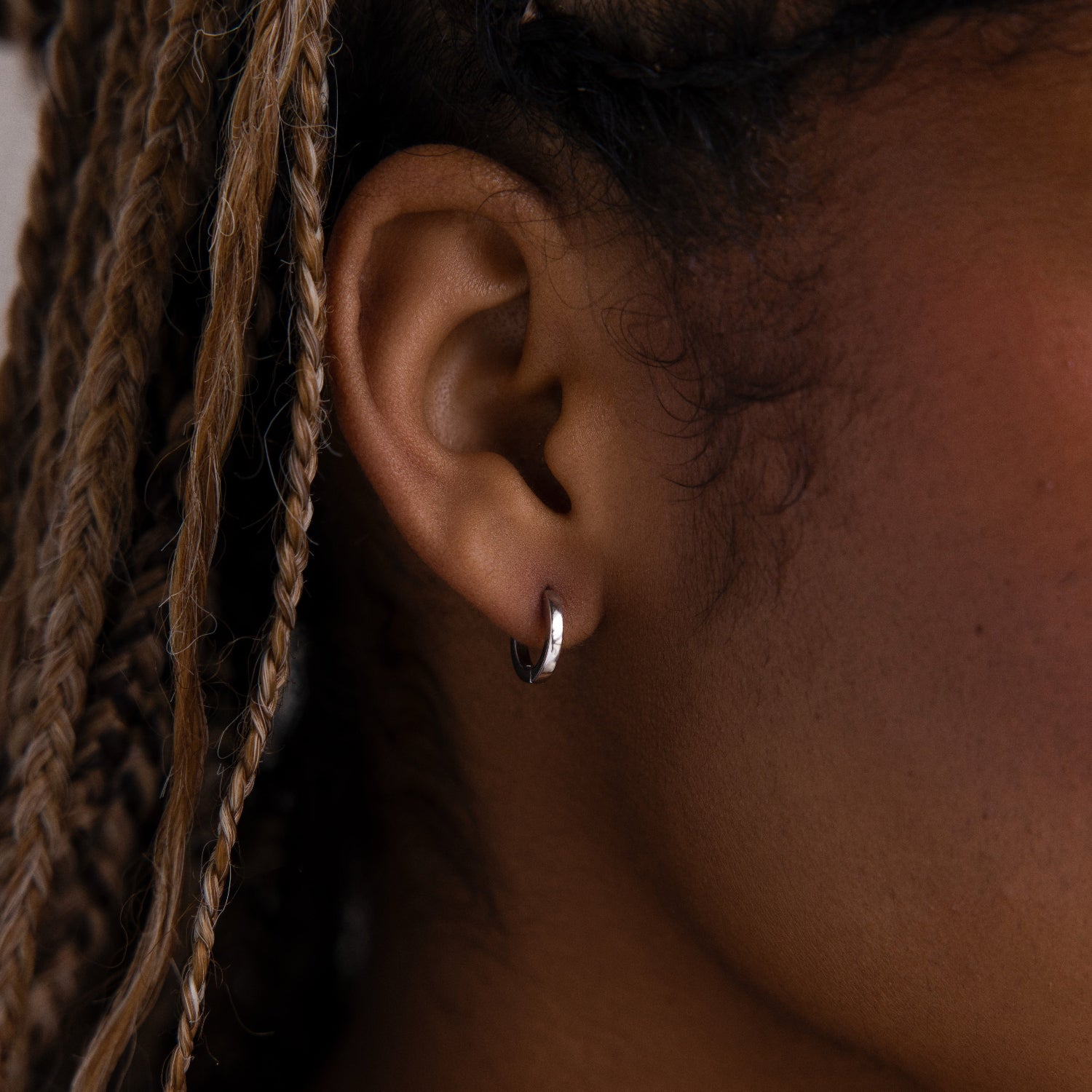 Close-up of an ear with a silver hoop earring and braided hair.