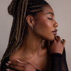 Woman with braided hair wearing various silver hoop earrings against a neutral background