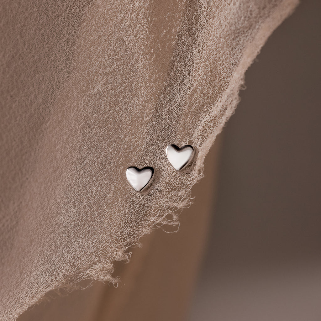 Heart-shaped silver stud earrings on a textured beige surface
