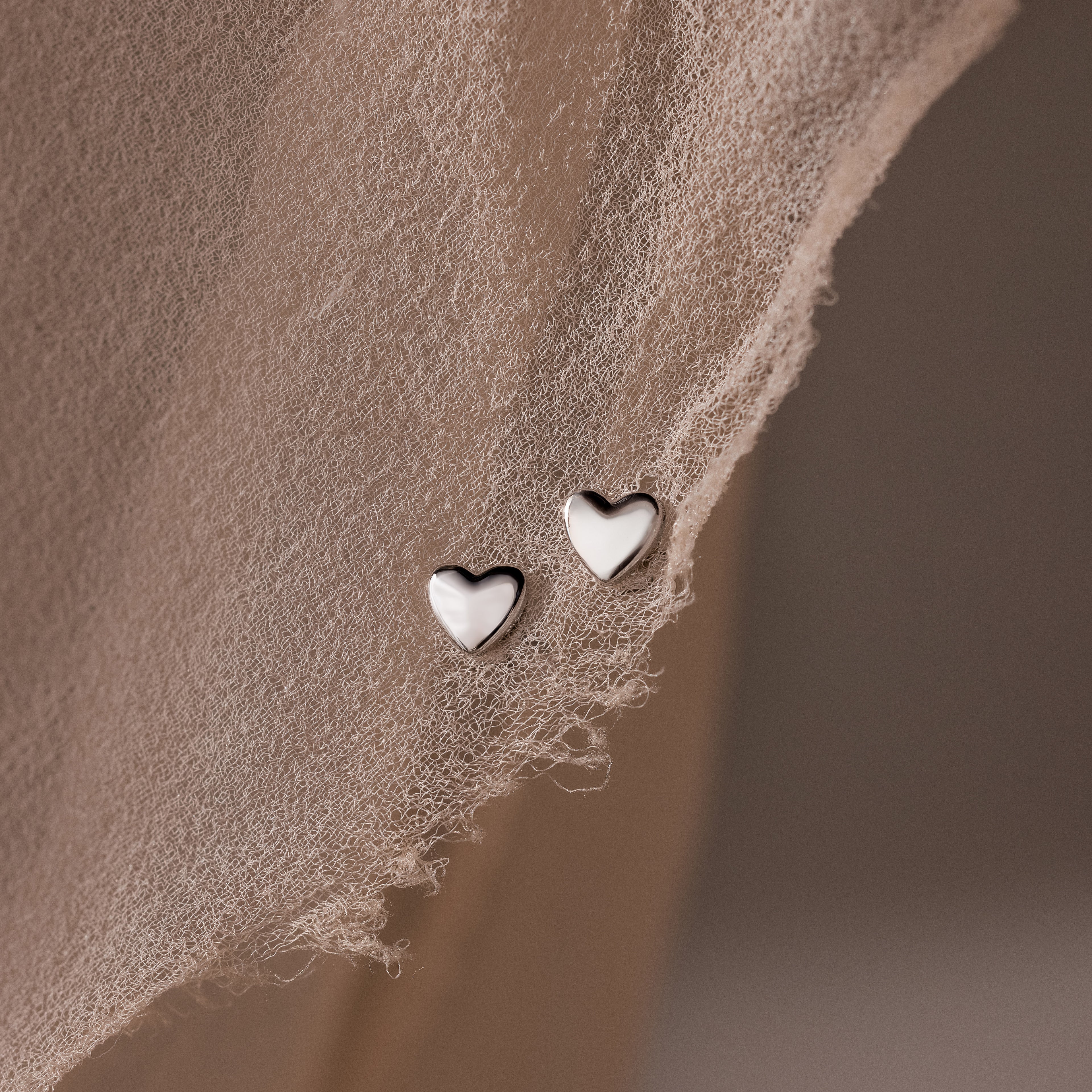 Heart-shaped silver stud earrings on a textured beige surface