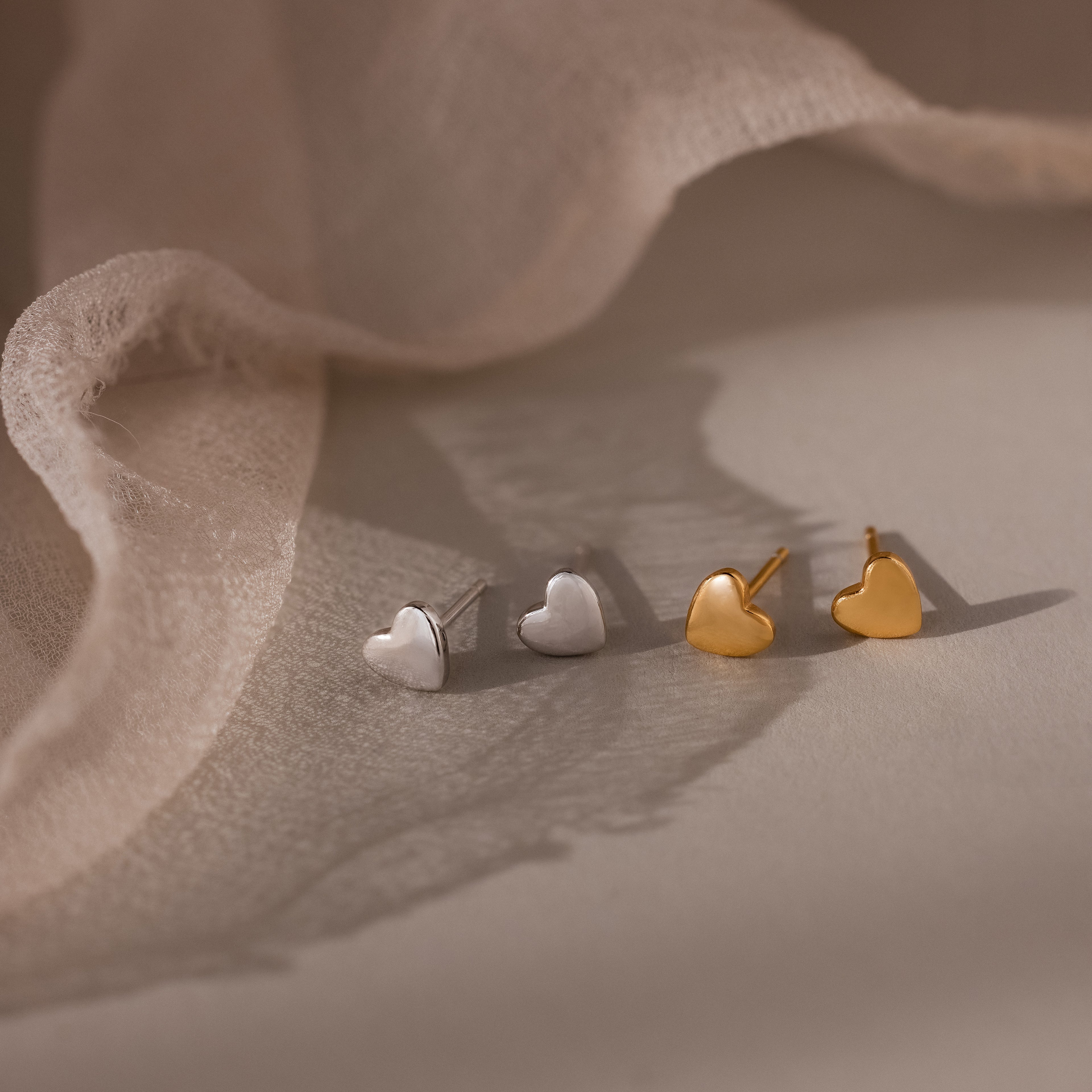 Heart-shaped earrings in silver and gold on a soft fabric background