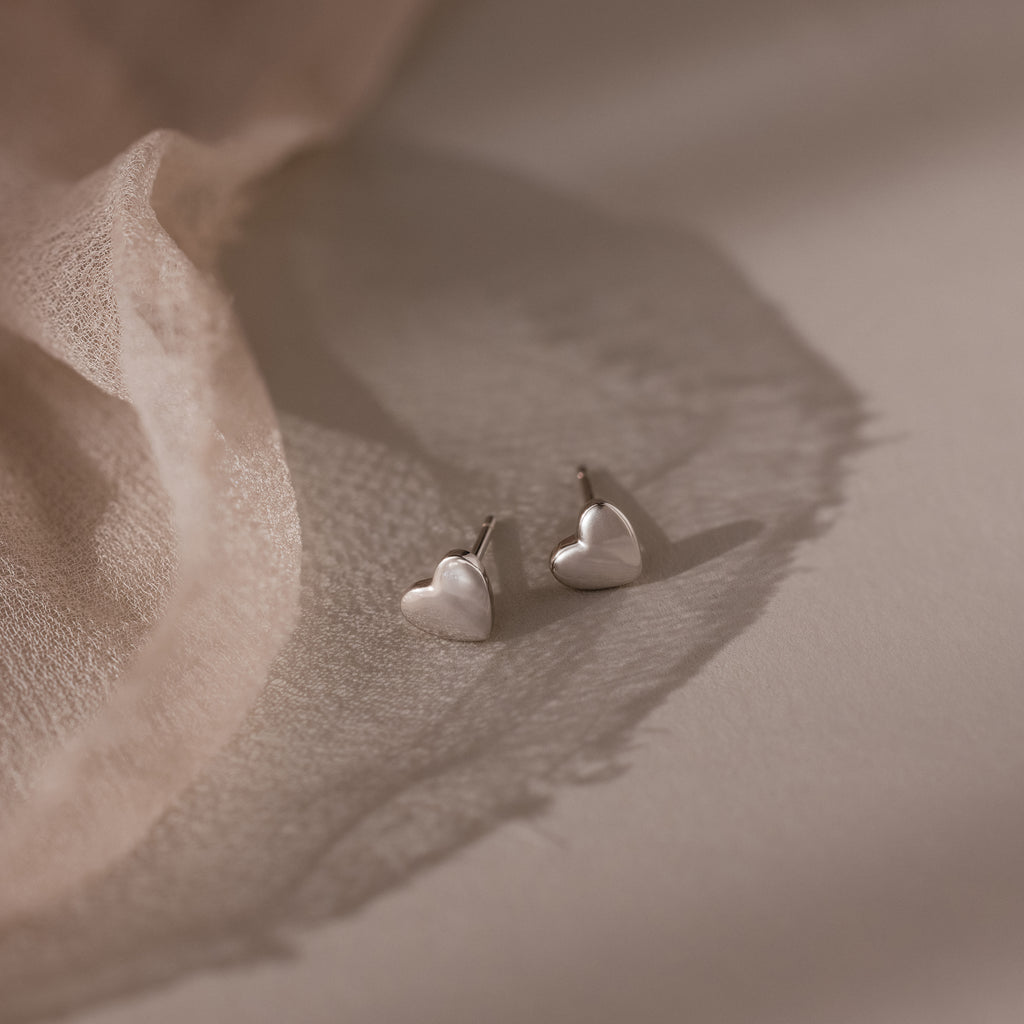 Heart-shaped silver stud earrings on a soft fabric background