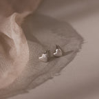 Heart-shaped silver stud earrings on a soft fabric background