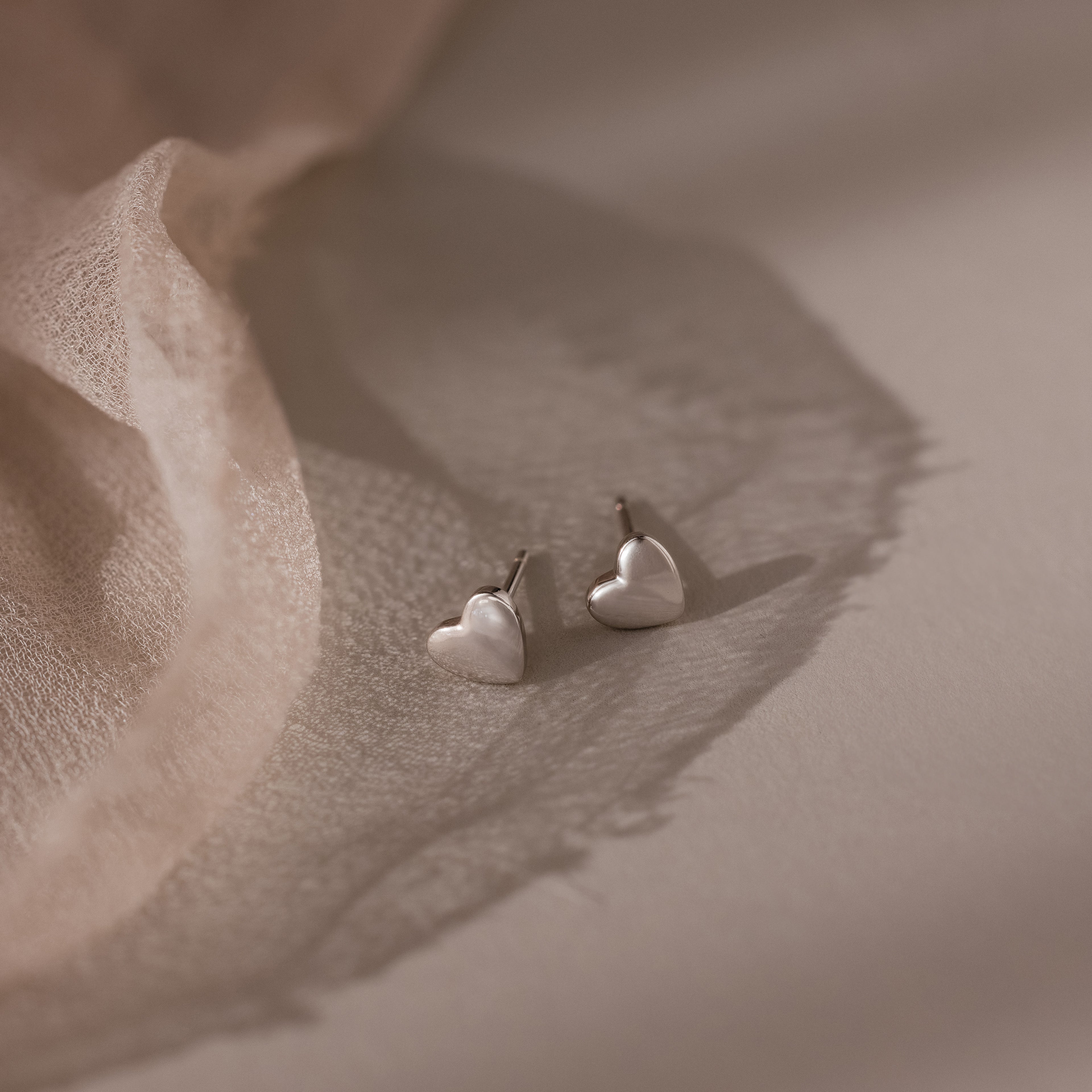 Heart-shaped silver stud earrings on a soft fabric background