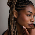 Woman with braided hair and a silver heart shaped stud earring touching her face against a neutral background