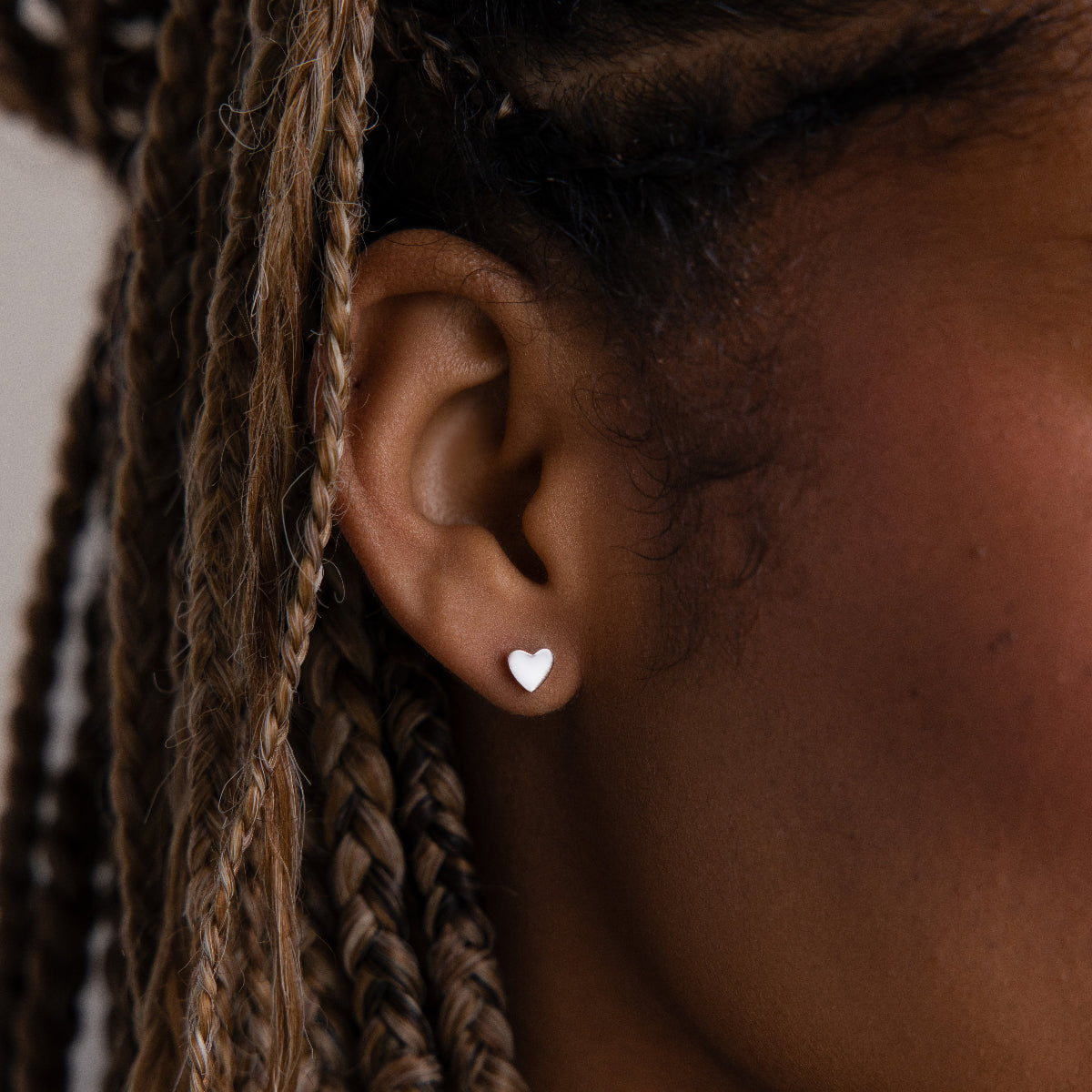 Close-up of an model with a silver heart-shaped stud earring and braided hair.