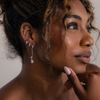 Close-up of a woman wearing various silver earrings with a neutral background