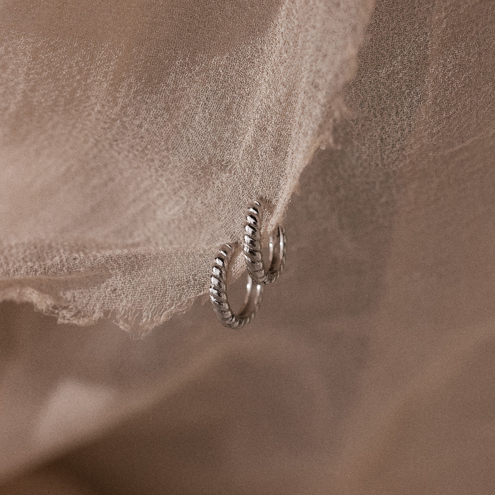 Silver twisted hoop earrings on a textured beige fabric background