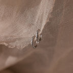 Silver twisted hoop earrings on a textured beige fabric background