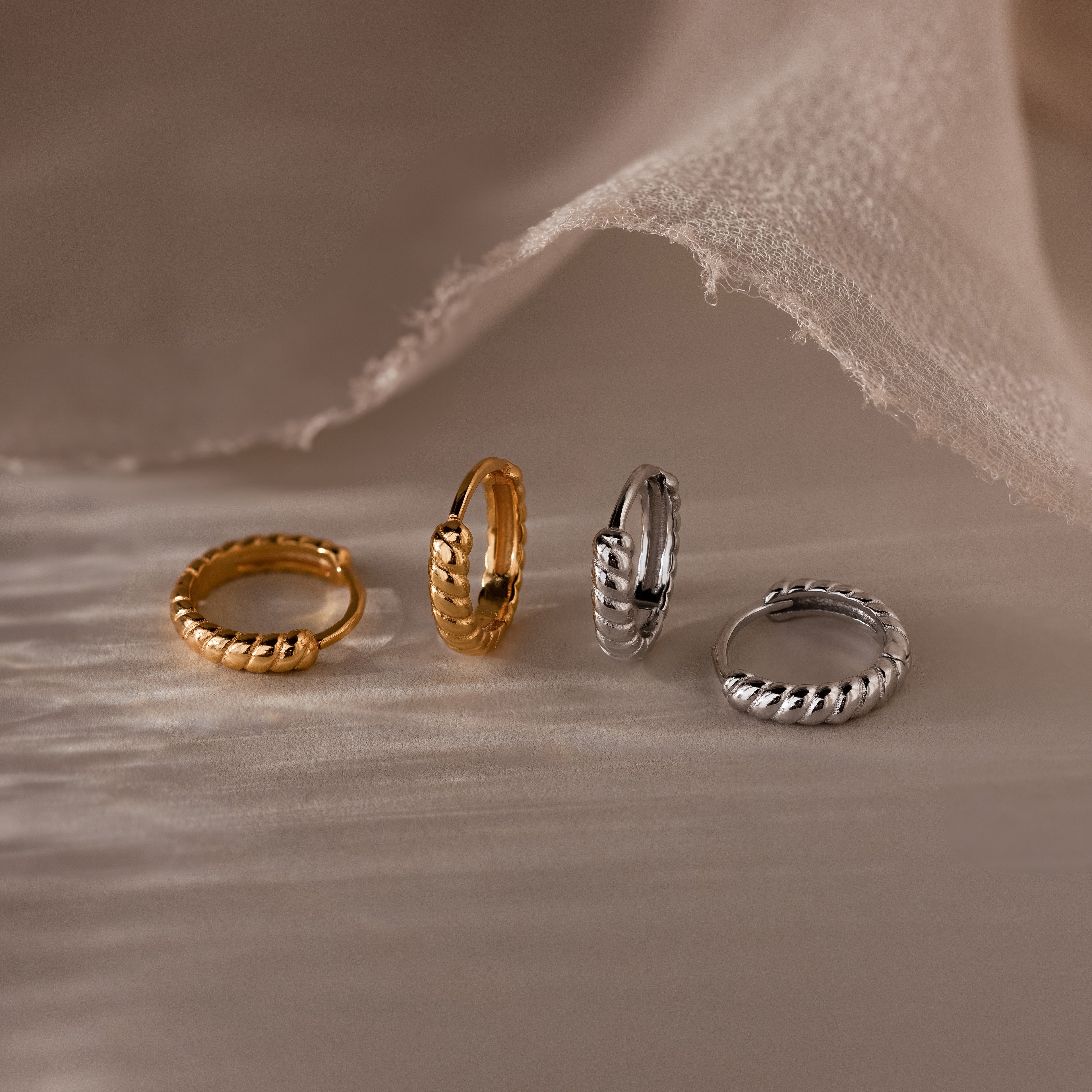 Four gold and silver hoop earrings on a textured beige surface