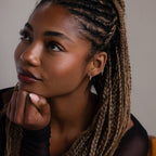 Woman with braided hair and a silver twisted hoop earring resting her chin on her hand against a neutral background