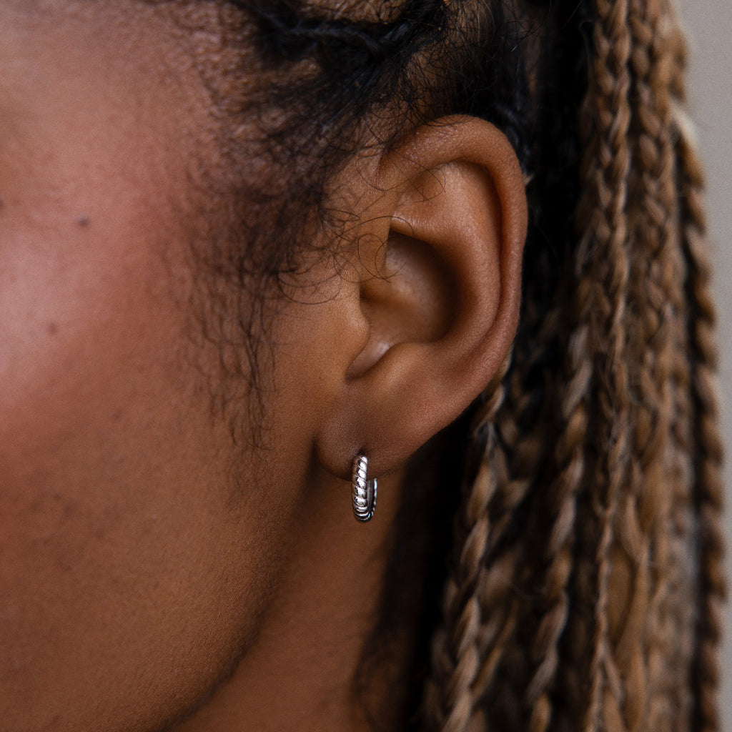 Close-up of an ear with a twisted hoop earring, focusing on the jewelry.
