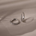 Pair of silver pave diamond hoop earrings on a beige fabric background