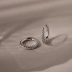 Pair of silver pave diamond hoop earrings on a beige fabric background