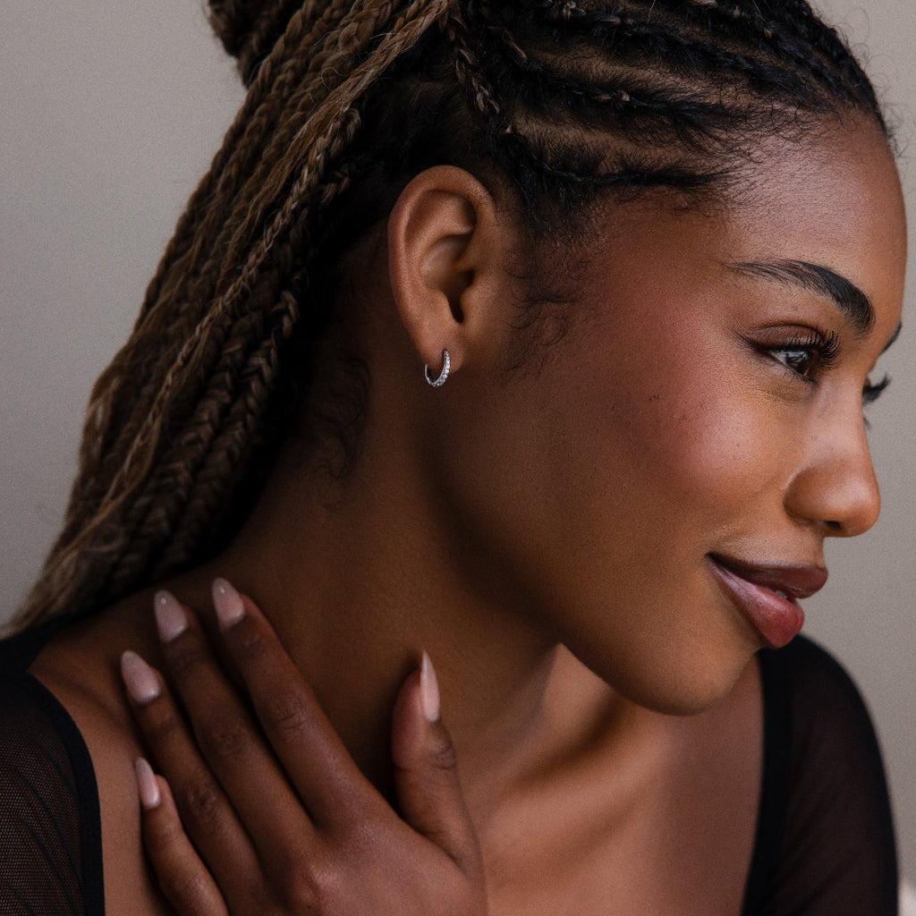Woman with braided hair wearing silver diamond hoop earrings, looking away from the camera.